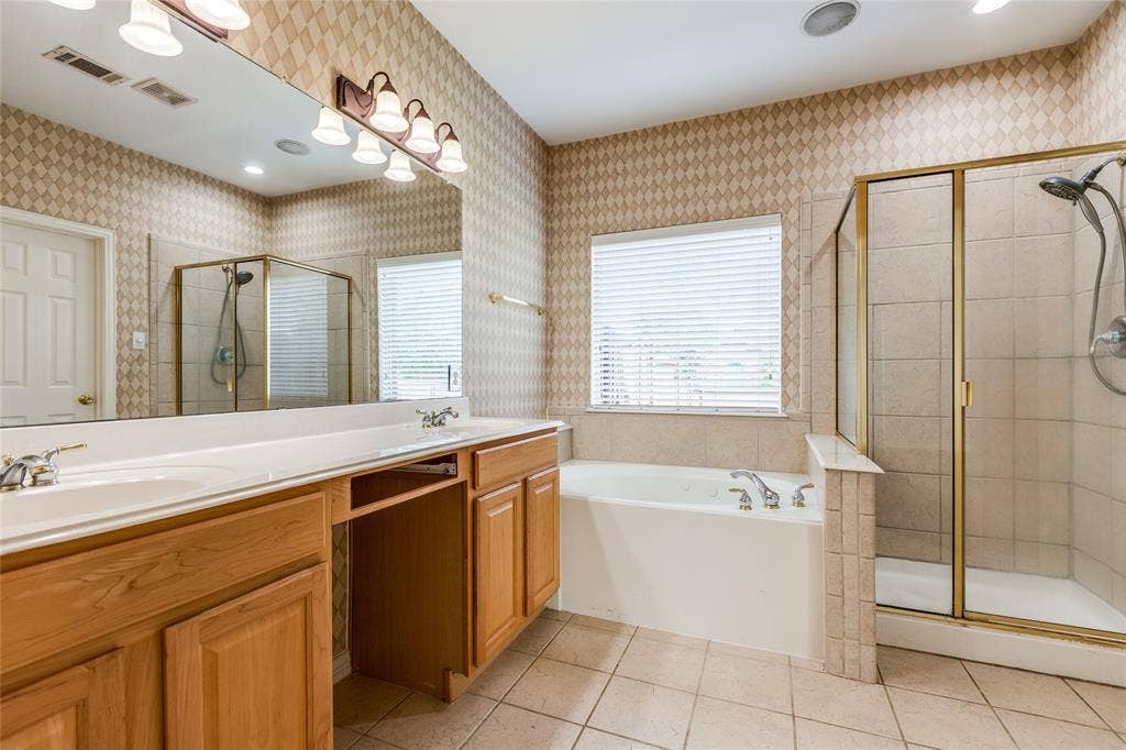 3401 Maddock Drive, McKinney, TX 75070 Spa-inspired master bathroom featuring dual vanity with wood cabinetry and ample countertop space, large soaker tub positioned beneath a transom window, walk-in shower with frameless glass enclosure and tile surround, recessed lighting, and neutral tile flooring throughout