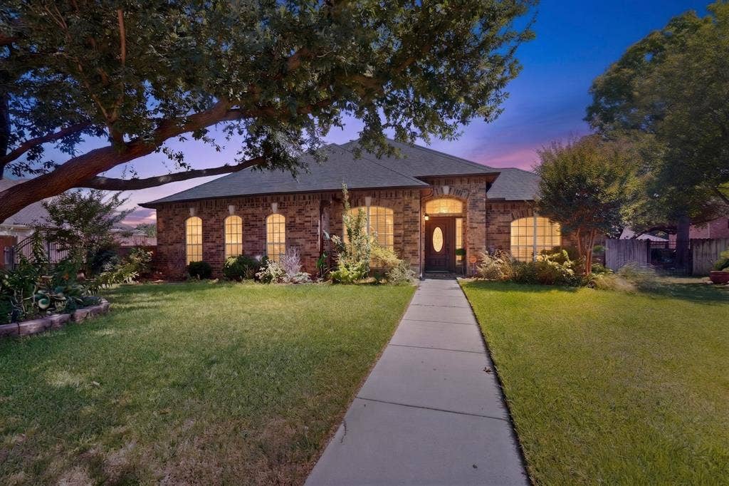 713 Mockingbird Court, Crowley, TX 76036 Brick facade residence featuring arched windows, a dark wood entry door with an oval glass insert, a concrete walkway, and mature trees