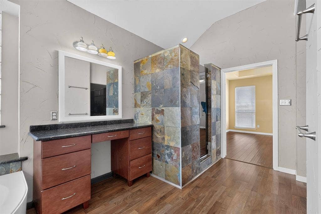 713 Mockingbird Court, Crowley, TX 76036 Wood-finish flooring, vanity with built-in cabinetry, dark countertop, framed mirror, and a tiled shower enclosure