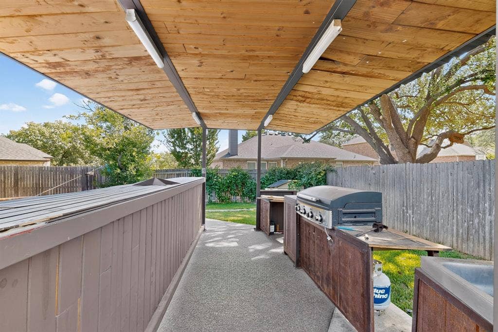 713 Mockingbird Court, Crowley, TX 76036 Covered outdoor kitchen featuring a built-in grill, integrated sink, and an expansive wood-slat ceiling with recessed lighting