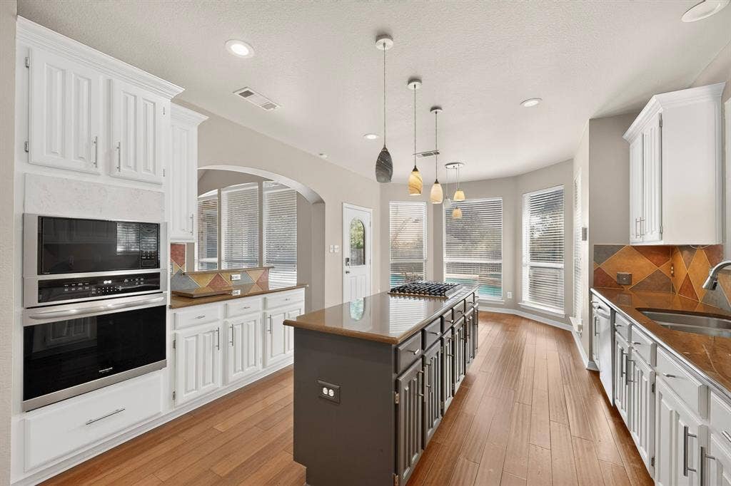 713 Mockingbird Court, Crowley, TX 76036 Kitchen featuring wood-finish flooring, white cabinetry, integrated stainless steel appliances, a center island with cooktop, and a bay window