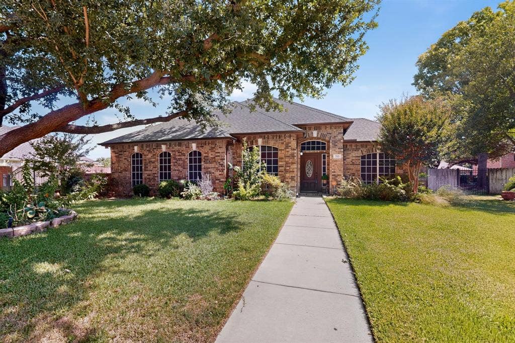713 Mockingbird Court, Crowley, TX 76036 Brick exterior with a dark-pitched roof, arched windows, an ornate front door, a concrete walkway, and mature trees