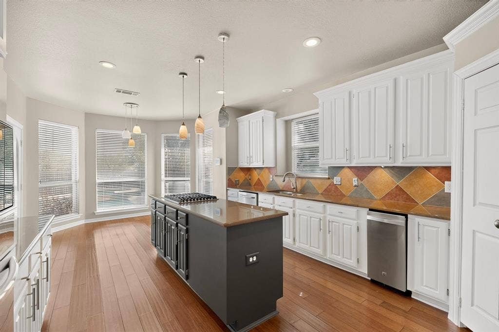713 Mockingbird Court, Crowley, TX 76036 Kitchen featuring wood-finish flooring, white cabinetry, a tiled backsplash, and an island with an integrated cooktop and pendant lighting