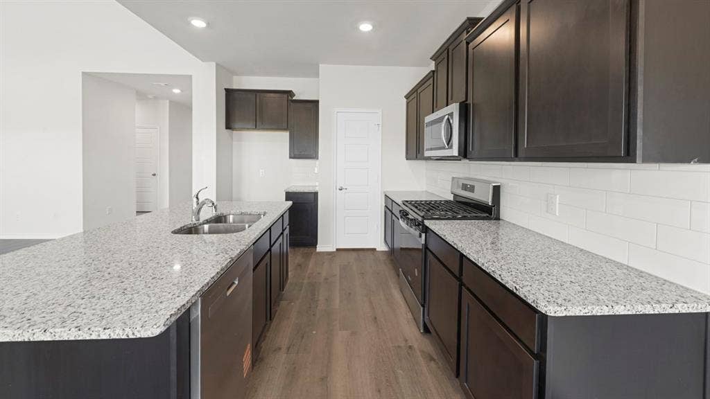 8425 Everly Drive, Garland, TX 75043 Galley-style kitchen featuring dark cabinetry, speckled quartz countertops, stainless steel appliances including a gas cooktop and built-in microwave, subway tile backsplash, and wood-finish flooring throughout