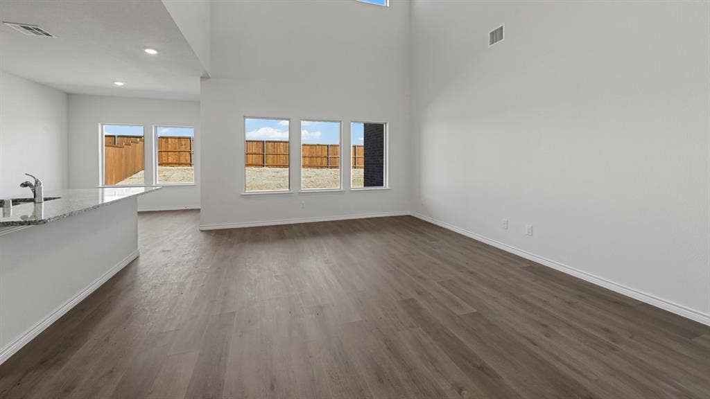 8425 Everly Drive, Garland, TX 75043 Open concept living area featuring high ceilings, recessed lighting, wood-finish flooring, a kitchen island with a stone countertop, and multiple windows with outdoor views
