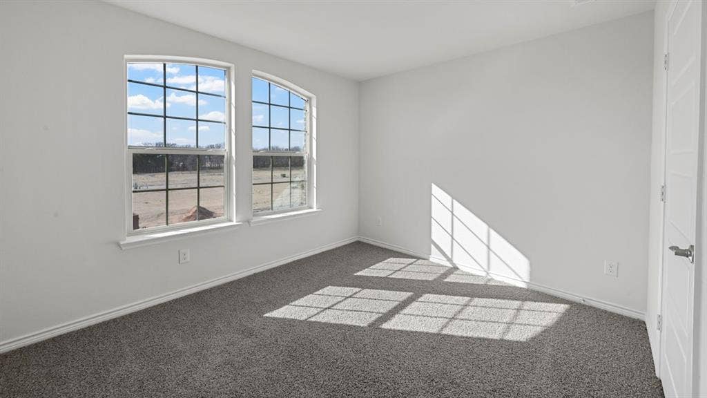 8425 Everly Drive, Garland, TX 75043 Bright room featuring two arched windows with grid patterns, light gray carpet, white walls, and a modern white paneled door with a brushed nickel handle