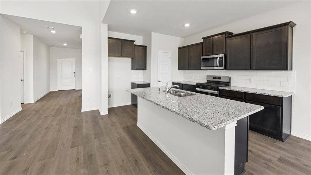 8425 Everly Drive, Garland, TX 75043 Kitchen featuring a granite island, dark wood-finish cabinetry, stainless steel appliances, a subway tile backsplash, and wood-finish flooring