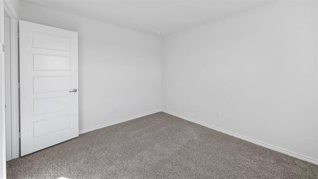 8425 Everly Drive, Garland, TX 75043 Spacious bedroom featuring neutral wall finishes, a clean white six-panel entry door, and soft gray carpet flooring throughout