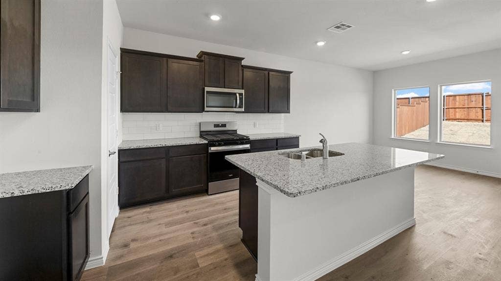 8425 Everly Drive, Garland, TX 75043 Modern kitchen featuring dark cabinetry, stainless steel appliances, and a spacious island with quartz countertop