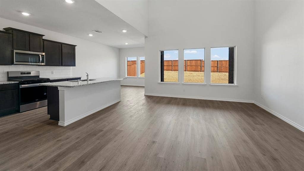 8425 Everly Drive, Garland, TX 75043 Spacious common area featuring wood-finish flooring, a kitchen island with sink, dark cabinetry, stainless steel appliances, and multiple windows