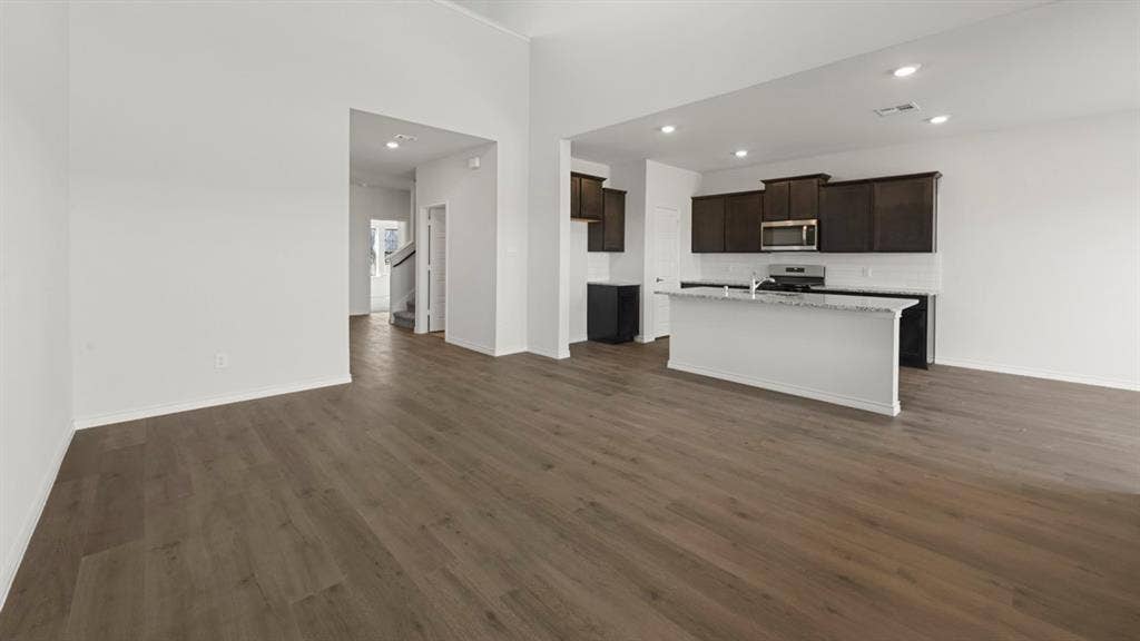8425 Everly Drive, Garland, TX 75043 Open-concept living space featuring wood-finish flooring, a kitchen island with stone countertop, dark cabinetry, stainless steel appliances, and recessed lighting