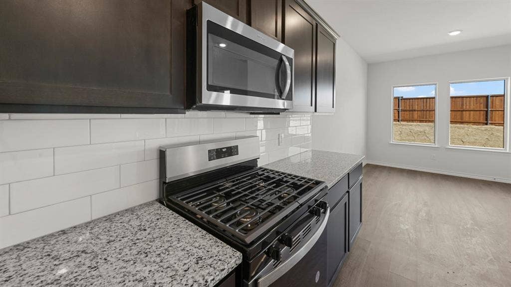8425 Everly Drive, Garland, TX 75043 Kitchen featuring stainless steel appliances, granite-style countertops, dark wood-finish cabinetry, and a subway tile backsplash