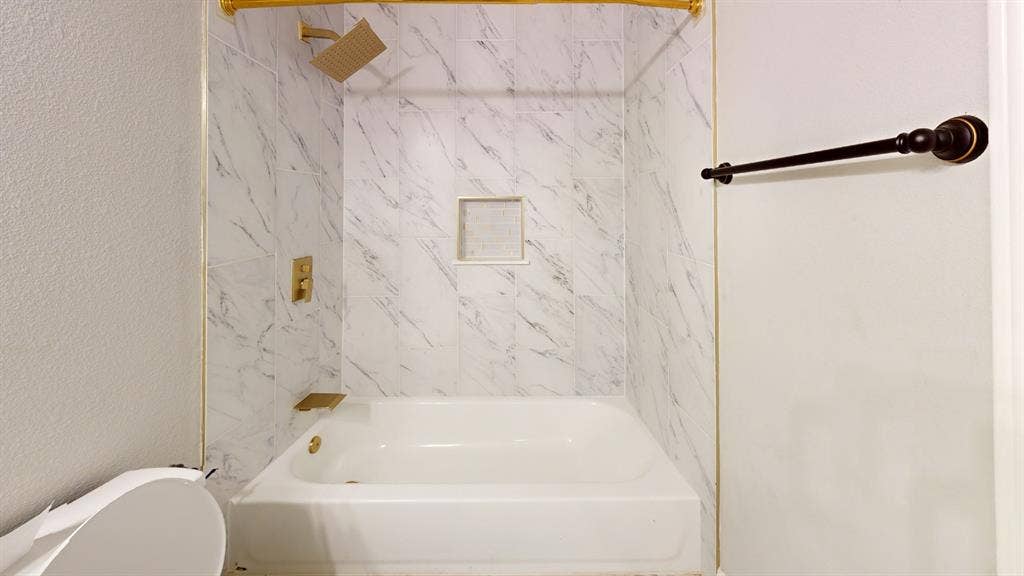 3312 Woodberry Lane, McKinney, TX 75071 Bathtub with white subway tile surround, gold-finish fixtures, and a recessed shower niche