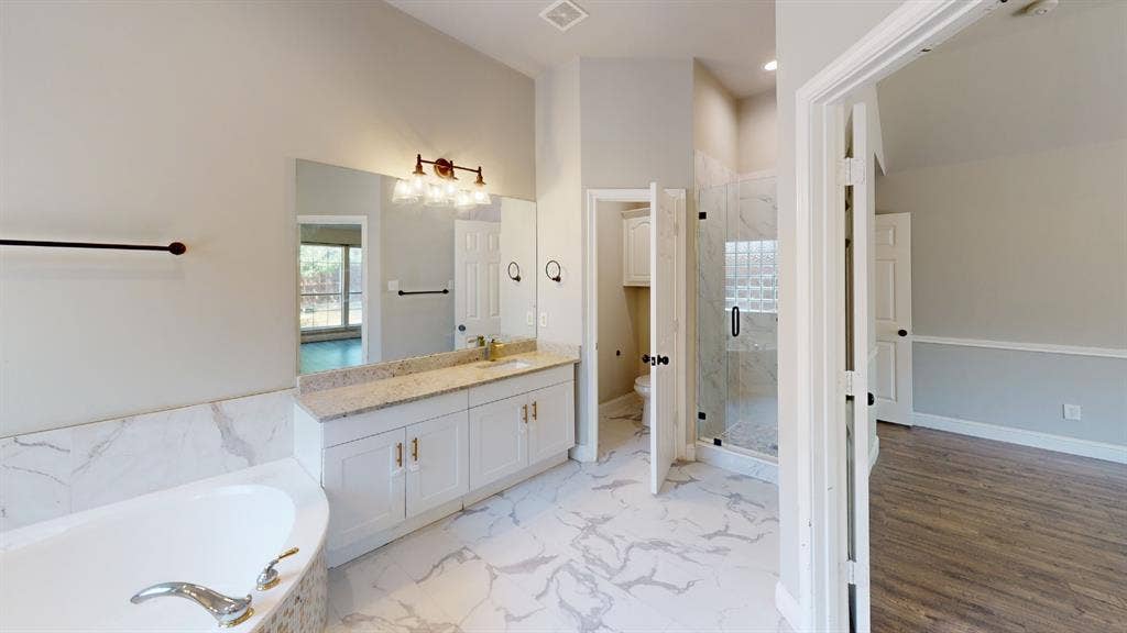 3312 Woodberry Lane, McKinney, TX 75071 Spacious bathroom featuring a large soaking tub with tile surround, a double vanity with stone countertop and ample storage, an enclosed shower with glass doors, and elegant tile flooring