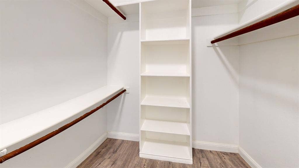 3312 Woodberry Lane, McKinney, TX 75071 Spacious walk-in closet featuring dual clothing rods with ample hanging space, a central shelving unit with multiple compartments for organized storage, and wood-finish flooring throughout