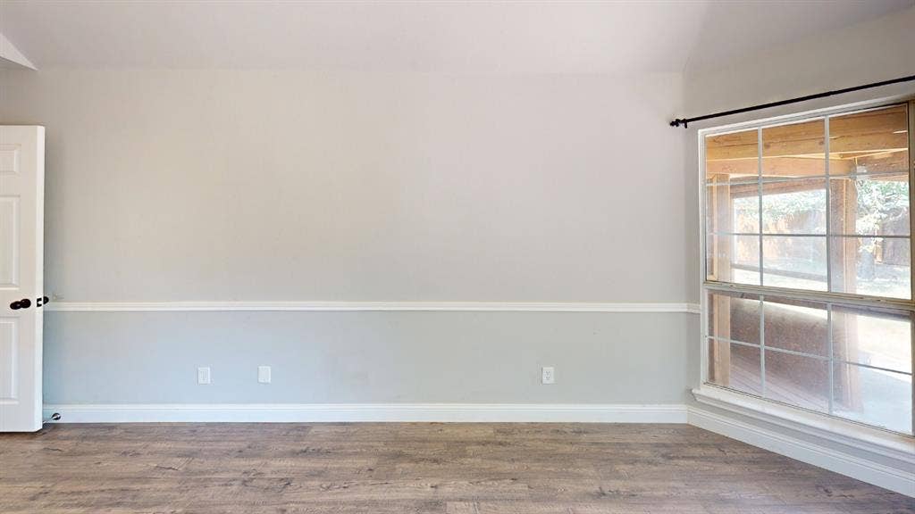 3312 Woodberry Lane, McKinney, TX 75071 Spacious living area featuring wood-finish flooring, neutral two-tone wall treatment with chair rail detail, and abundant natural light from large windows with wood blinds