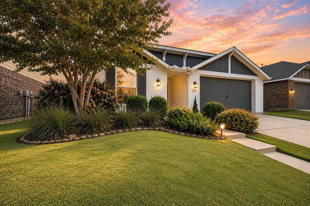 White brick exterior with dark gray siding accents, attached two-car garage, concrete driveway, and established front landscaping
