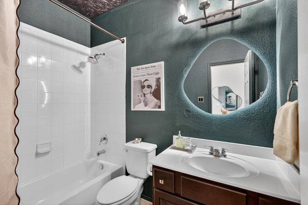 Bathroom featuring a white subway tile tub and shower combination, a dark wood-finish vanity with a white countertop and integrated sink, and an illuminated irregular-shaped mirror