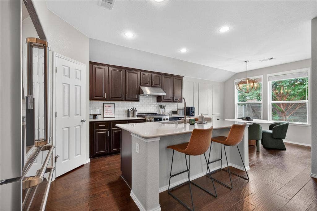 Modern kitchen featuring dark wood cabinetry, stainless steel appliances, and a white quartz island with waterfall edge