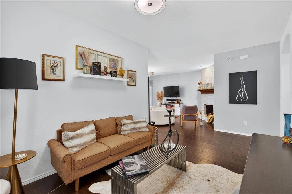 Bright, open living room showcasing warm wood-finish flooring, a rolled-arm sofa in cognac leather, and white walls accented by a charcoal feature wall