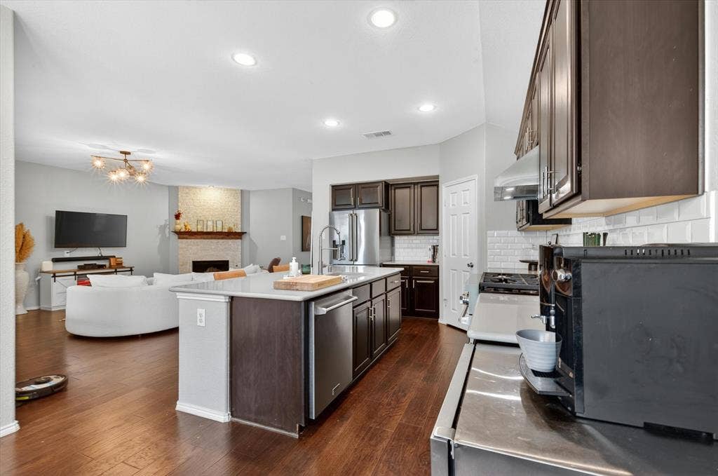 Open-concept kitchen and living area featuring a large center island with wood-finish countertop, dark cabinetry with stainless steel appliances, white subway tile backsplash, and recessed ceiling lighting