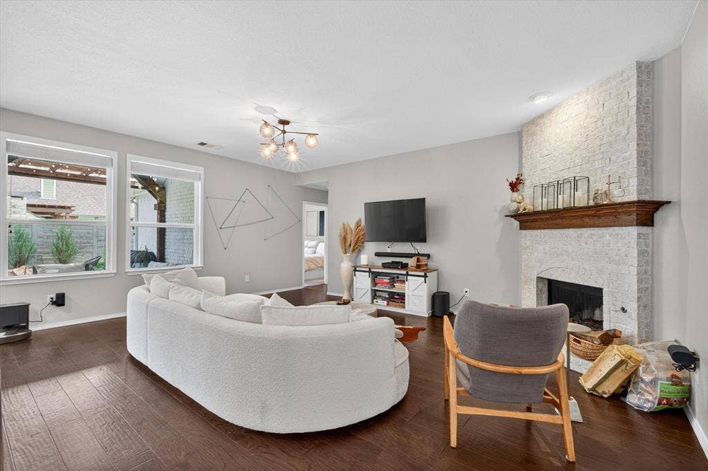 Living space with wood-finish flooring, a white brick fireplace with a wood mantel, and multiple windows