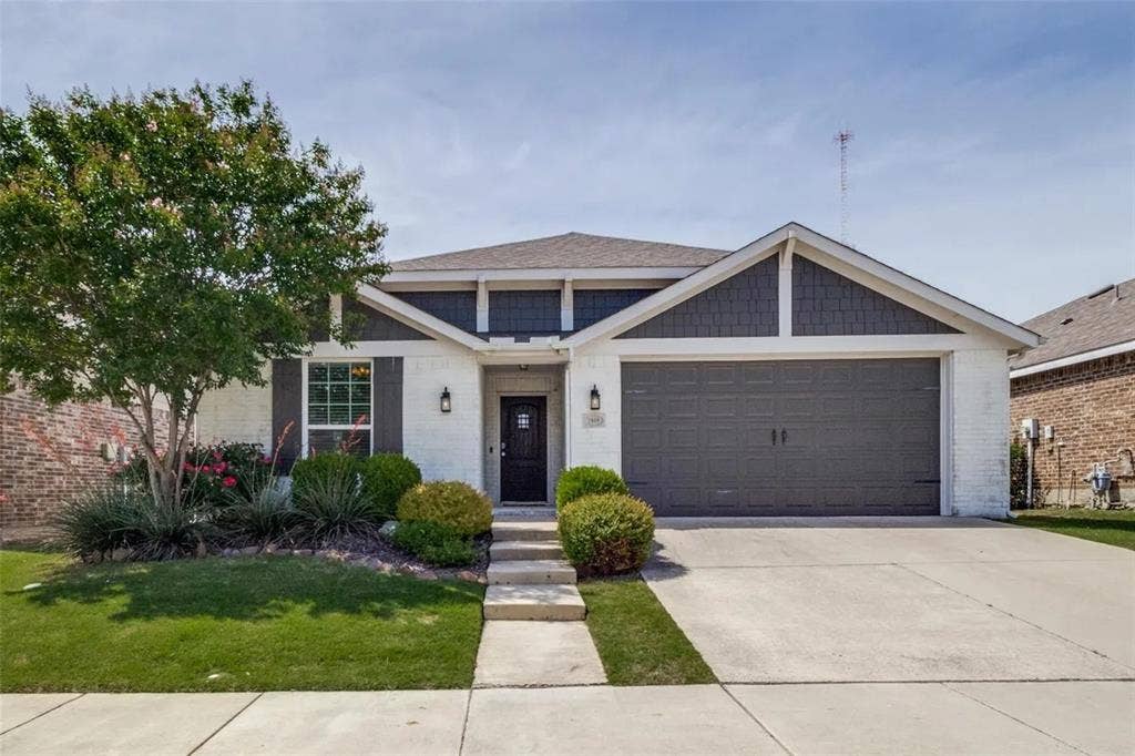 Charming single-story home featuring a crisp white and gray exterior with peaked gable roofline and brick accents