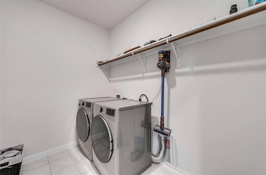 902 Western Way, Princeton, TX 75407 Modern laundry room featuring stacked front-load washer and dryer with chrome hardware, white subway tile flooring, and wall-mounted drying rod with integrated storage system