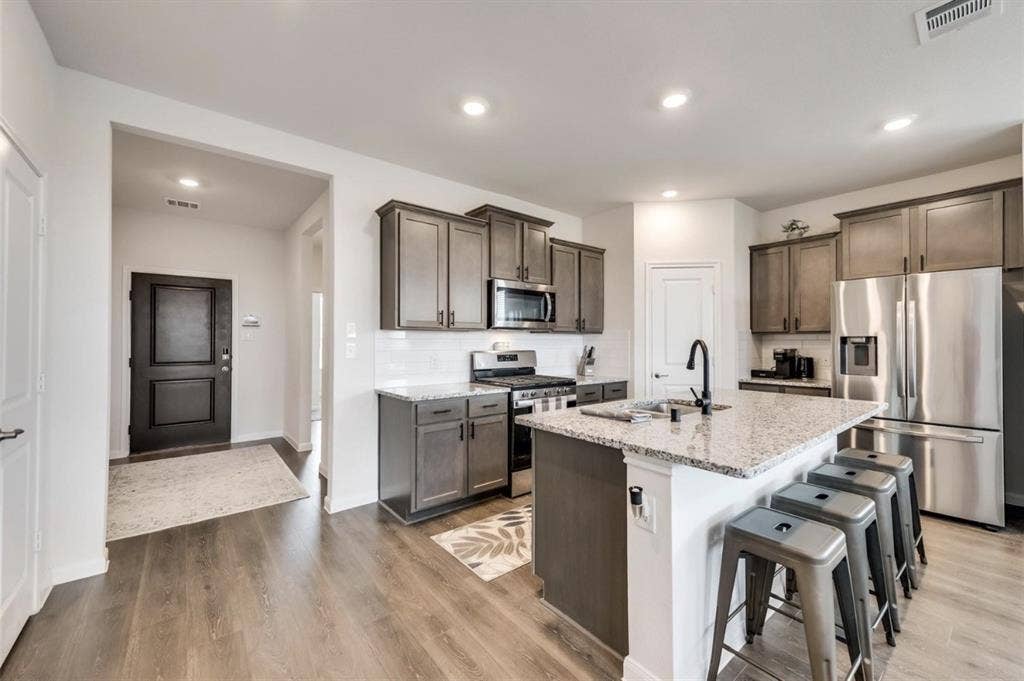 902 Western Way, Princeton, TX 75407 Kitchen with wood-finish flooring, recessed lighting, white subway tile backsplash, stainless steel appliances, and a central island featuring a stone countertop and seating area