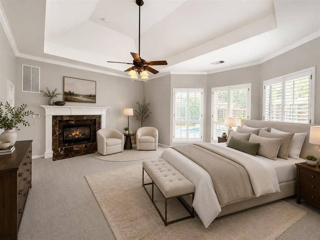 Spacious room with a tray ceiling and ceiling fan, featuring a fireplace with a white mantel and dark marble surround