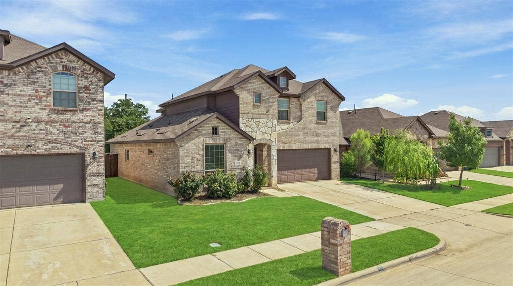 Two-story residence featuring a brick and stone facade, an attached two-car garage, manicured front lawn, a paved driveway, and mature landscaping
