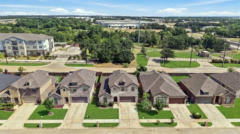 Residential street featuring multiple single-family homes with pitched roofs, brick and stone facades, and attached garages
