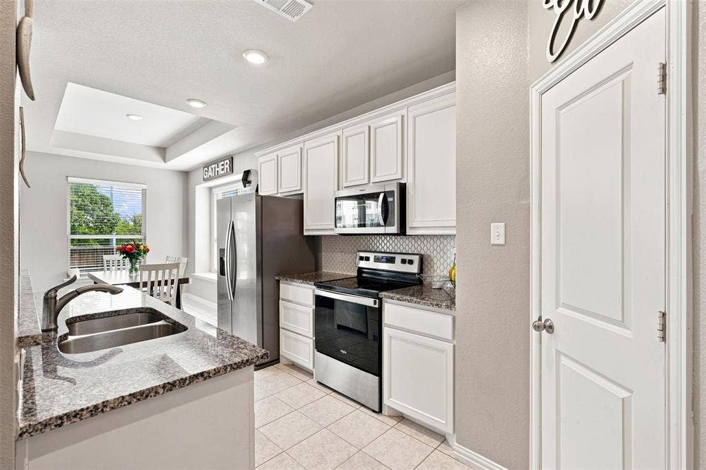 Kitchen featuring white cabinetry, stainless steel appliances, granite countertops, and a tiled backsplash