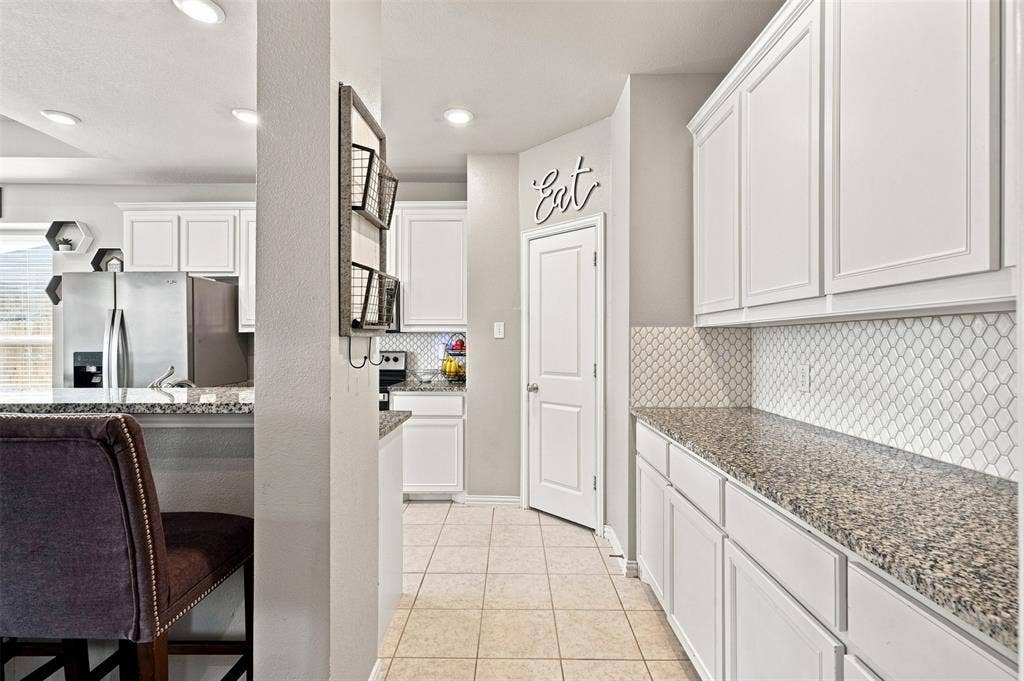 Kitchen featuring white cabinetry with crown molding, light-toned granite countertops, and a white patterned tile backsplash