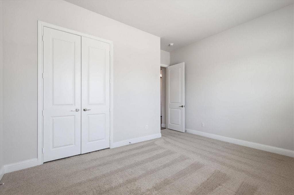 Neutral-toned carpeting featuring a textured pattern, complemented by white baseboards, light grey wall paint, and a two-panel bifold closet door