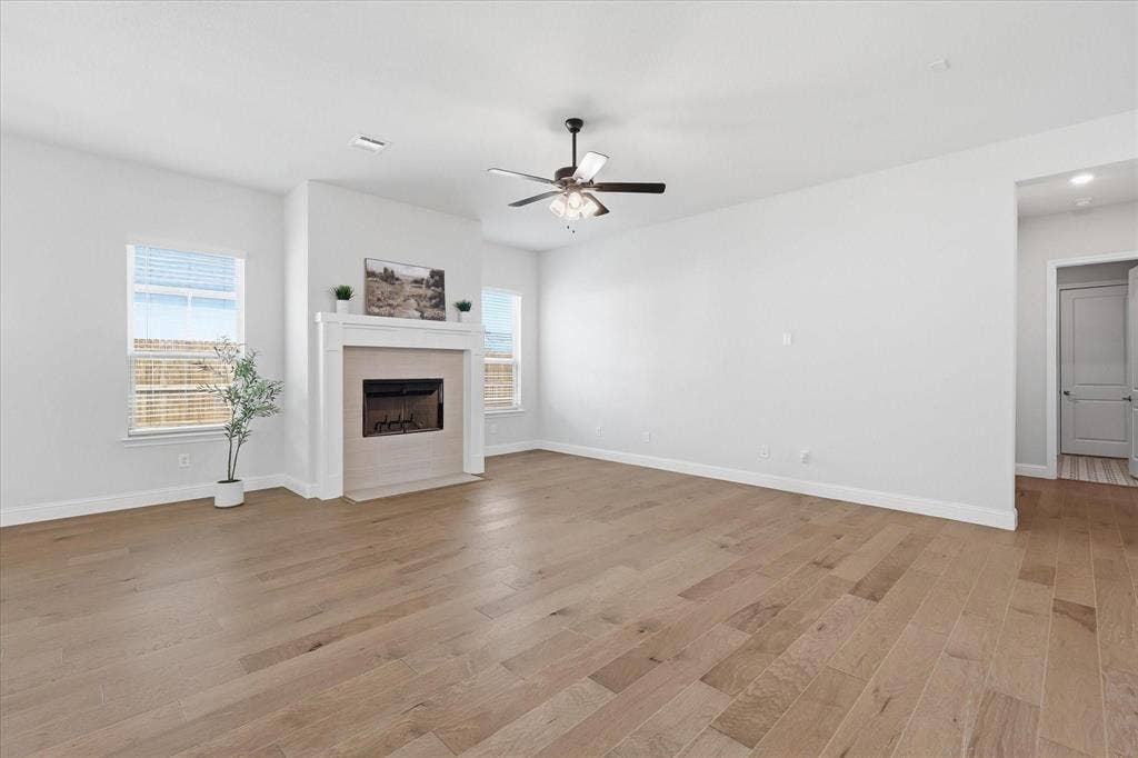 Expansive living space featuring light wood-finish flooring, a contemporary fireplace with a light-toned surround and mantel, and white walls
