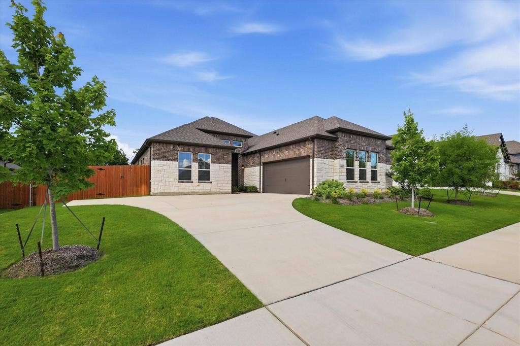 Brick and stone facade residence featuring a two-car garage, concrete driveway, and manicured landscaping with young trees