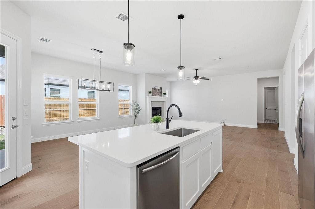 Open-concept living space featuring a white kitchen island with an undermount sink and stainless steel dishwasher, wood-finish flooring, multiple windows, a rear glass-paned door, and a fireplace with a mantel