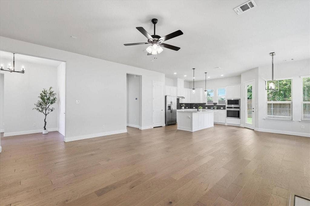 Spacious open-concept living area featuring light wood-finish flooring, a contemporary ceiling fan, and recessed lighting