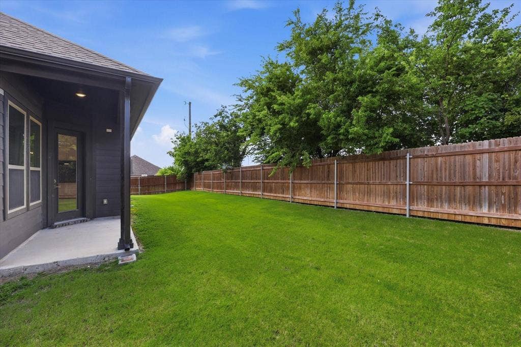 Spacious backyard featuring a manicured lawn, full-height privacy fence, and mature perimeter trees