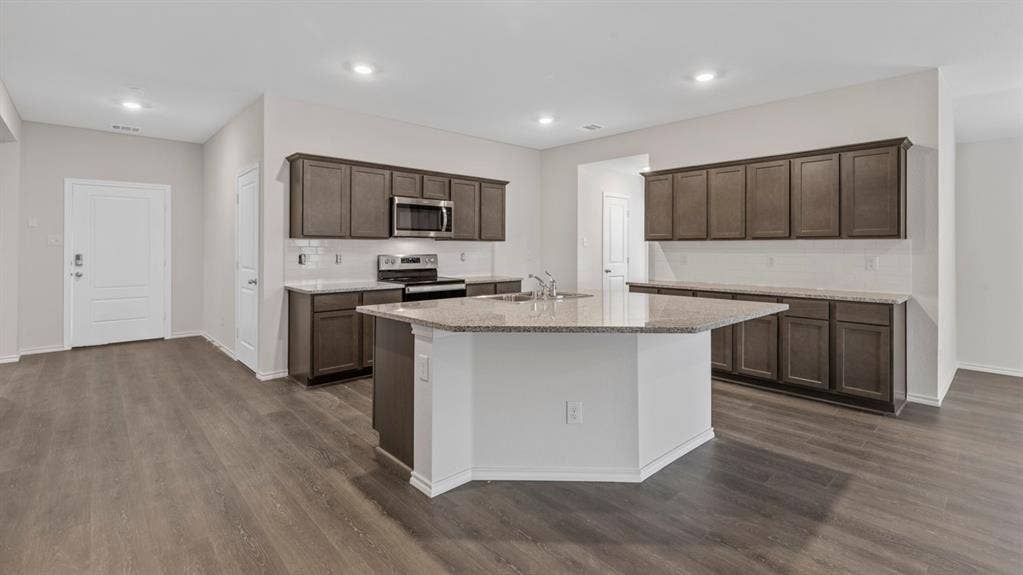 401 Banner Avenue, Royse City, TX 75189 Spacious kitchen featuring a large island with sink, ample cabinetry, granite-finish countertops, stainless steel appliances, and wood-finish flooring