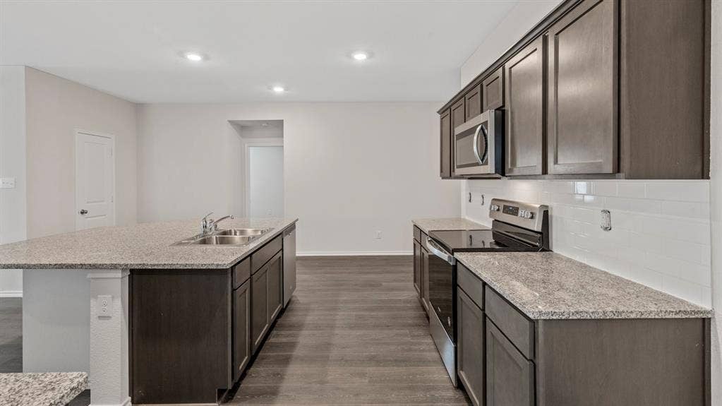 401 Banner Avenue, Royse City, TX 75189 Kitchen featuring dark wood-finish cabinetry, light speckled countertops, stainless steel appliances, and a subway tile backsplash