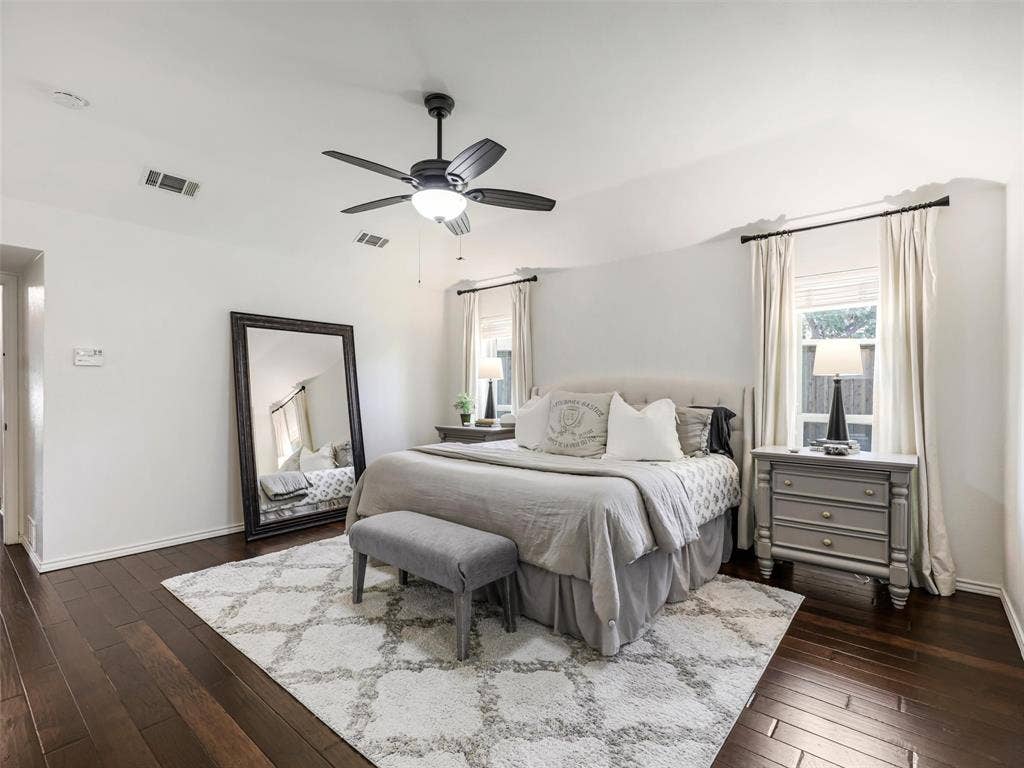 3617 Hackamore Court, Plano, TX 75023 Spacious bedroom featuring dark wood-finish flooring, a ceiling fan with integrated lighting, and two windows with blinds and drapery