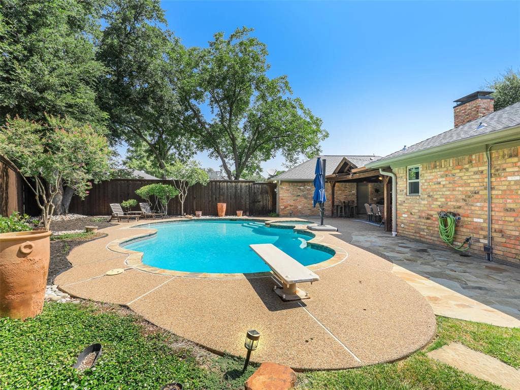 3617 Hackamore Court, Plano, TX 75023 Rear property featuring a kidney-shaped pool with a diving board, exposed aggregate decking, and a stone patio