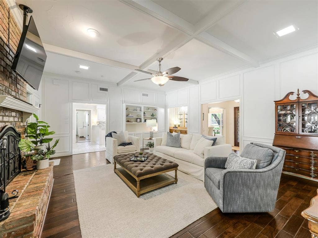 3617 Hackamore Court, Plano, TX 75023 Spacious living area featuring wood-finish flooring, a brick fireplace with a mantel, white paneled walls, and a coffered ceiling with a ceiling fan