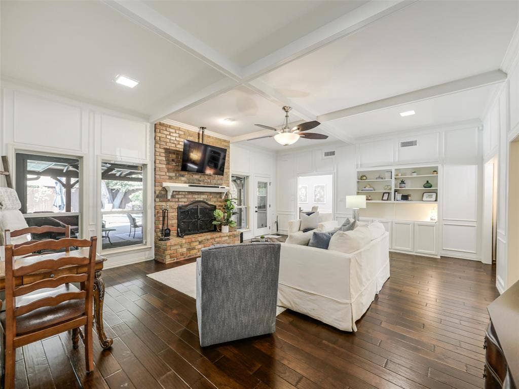 3617 Hackamore Court, Plano, TX 75023 Living area featuring wood-finish flooring, a brick fireplace with a white mantel, and built-in shelving with integrated lighting