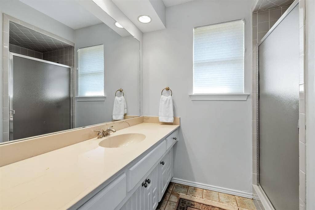 6803 Fernshaw Drive, Dallas, TX 75248 Dual vanity with an integrated sink and brushed nickel faucet, large wall mirror, recessed lighting, and a walk-in shower with frosted glass doors