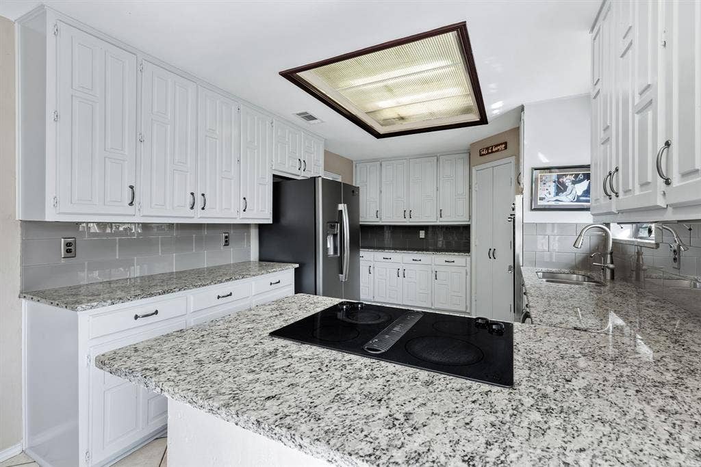 6803 Fernshaw Drive, Dallas, TX 75248 Kitchen featuring white cabinetry, light-toned countertops, a built-in electric cooktop, and a stainless steel refrigerator