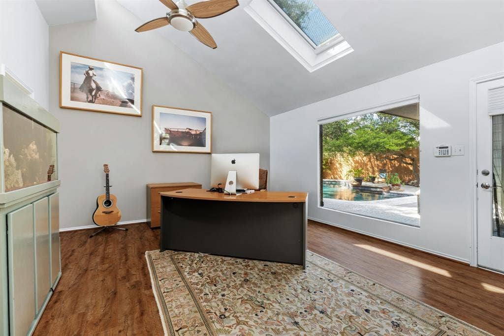 6803 Fernshaw Drive, Dallas, TX 75248 Bright, open office space featuring soaring vaulted ceilings with skylights, warm wood-finish flooring, and a large picture window framing outdoor scenery