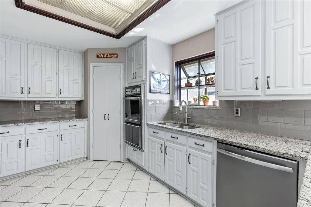 6803 Fernshaw Drive, Dallas, TX 75248 White cabinetry with dark hardware, stone countertops, stainless steel appliances, tile flooring, and a subway tile backsplash